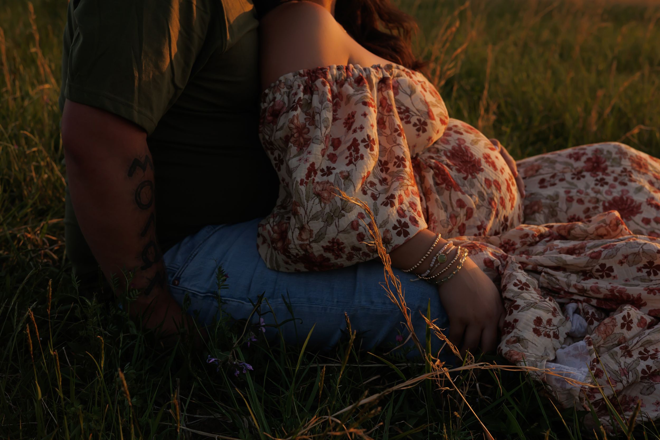 Intimate sunset portrait of couple sitting in tall grass field.