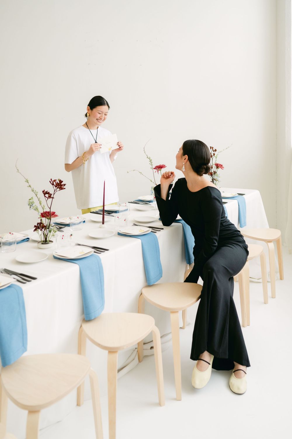 Two people in black and white outfits sit at an elegantly set table with light blue linens and floral arrangements.
