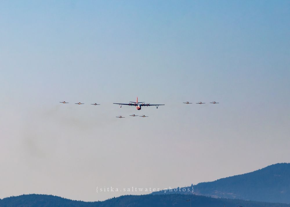 Hawaii Mars flying in formation with CF Snowbirds against a mountain backdrop during an aerial display.
