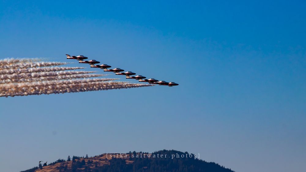 CF Snowbirds in formation creating diagonal smoke trails against blue sky.