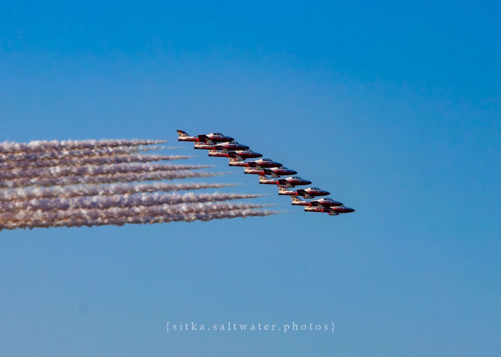 CF Snowbirds flying in formation leaving smoke trails against bright blue sky.