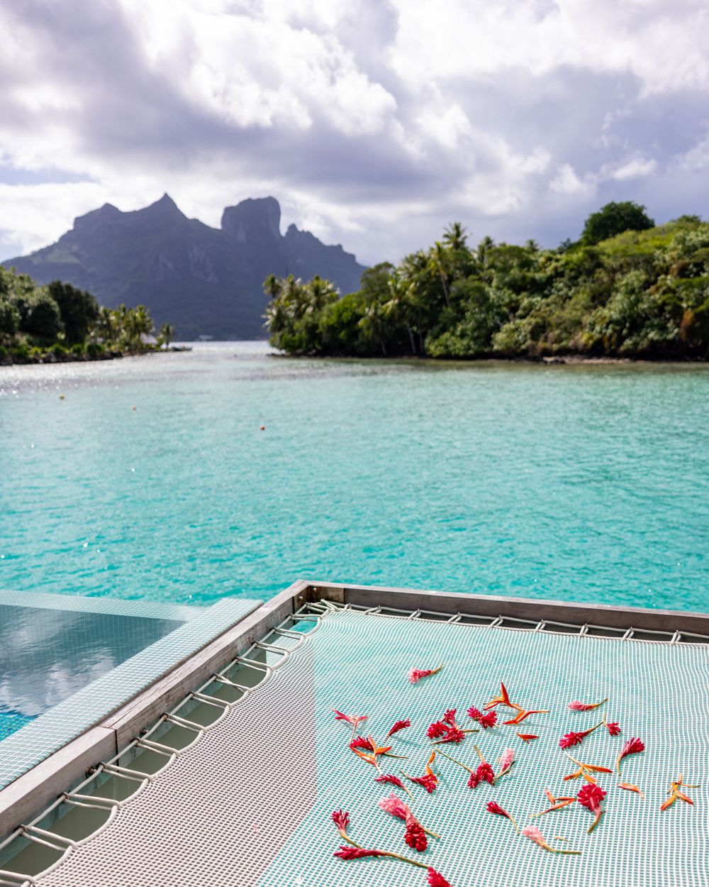 Infinity pool deck scattered with red flower petals overlooking stunning mountain peaks and lagoon views.