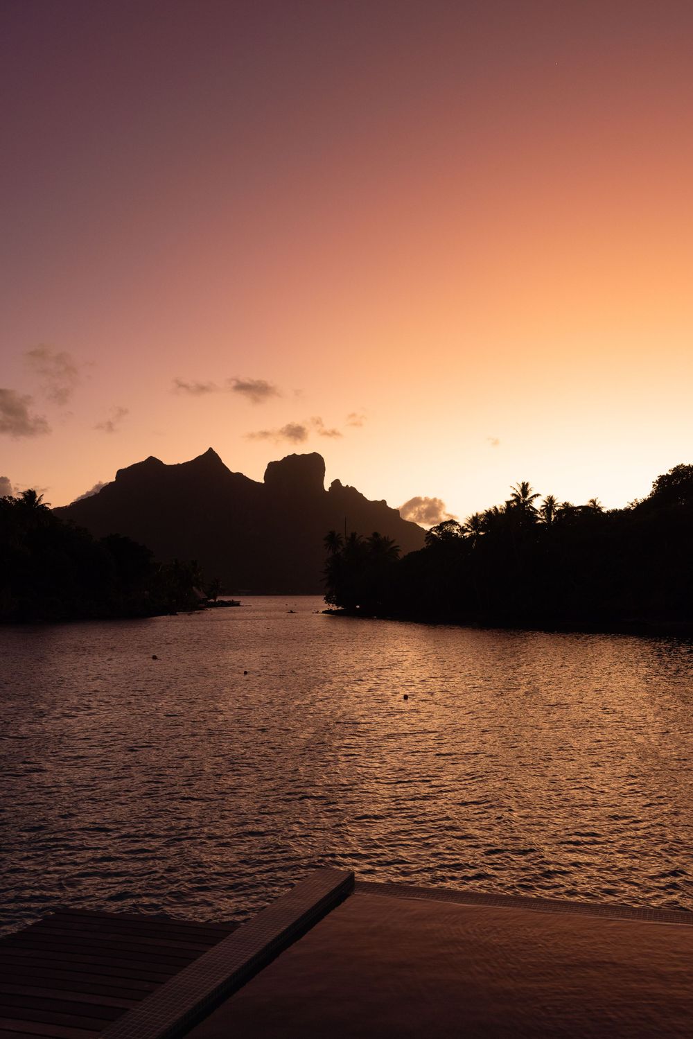 Dramatic sunset silhouette of mountains reflecting on calm water.