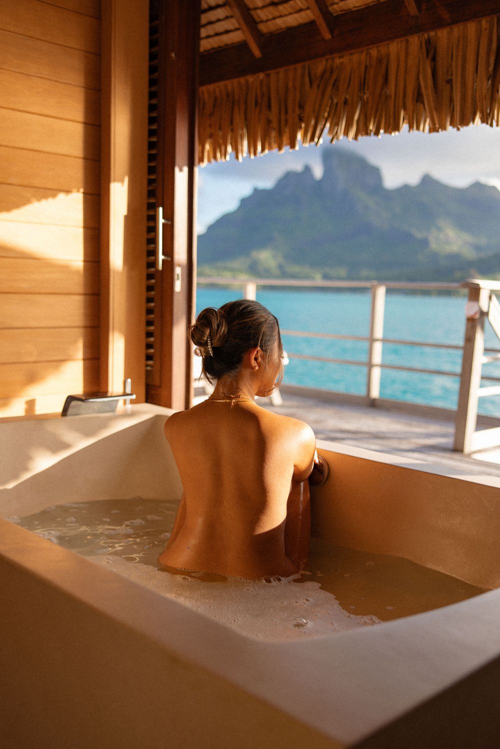 Luxurious bathtub overlooking pristine turquoise waters and mountain views at an overwater bungalow.