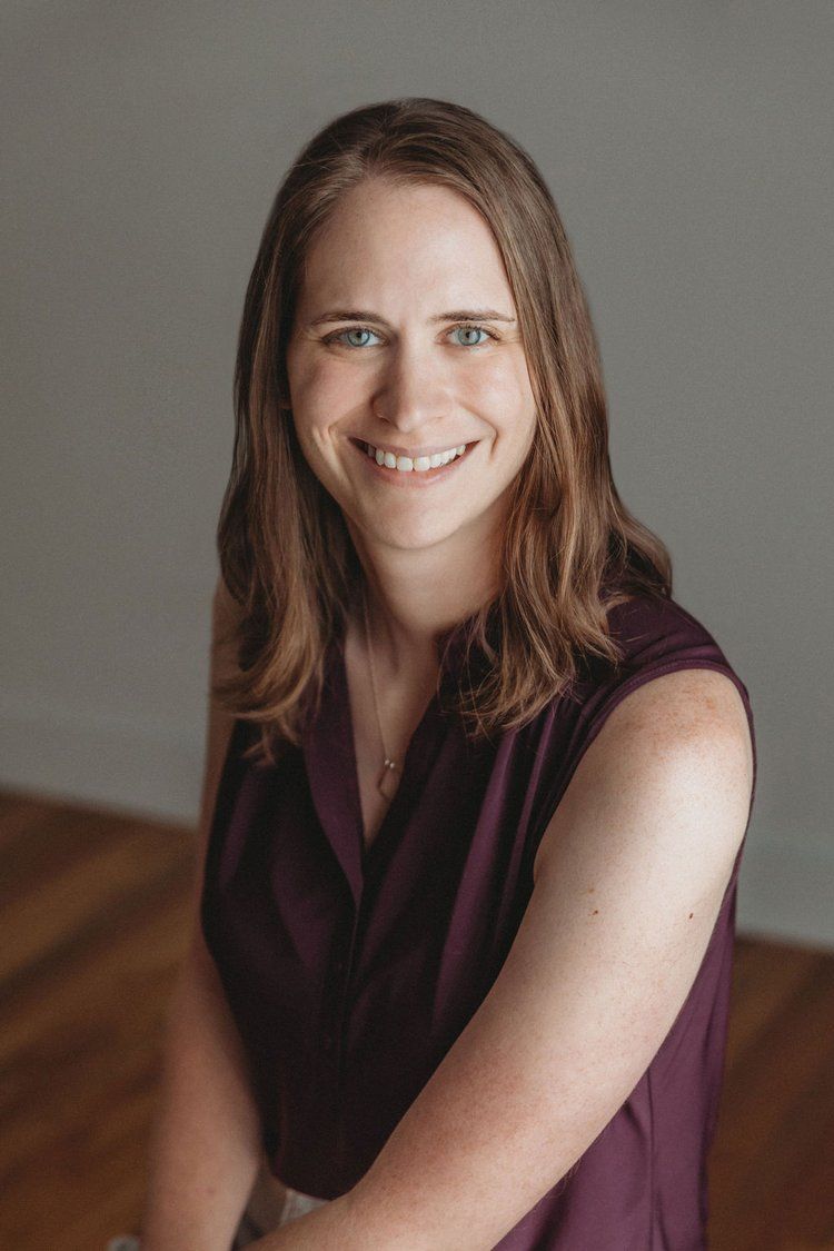 Professional portrait of someone in a burgundy sleeveless top against a neutral background.