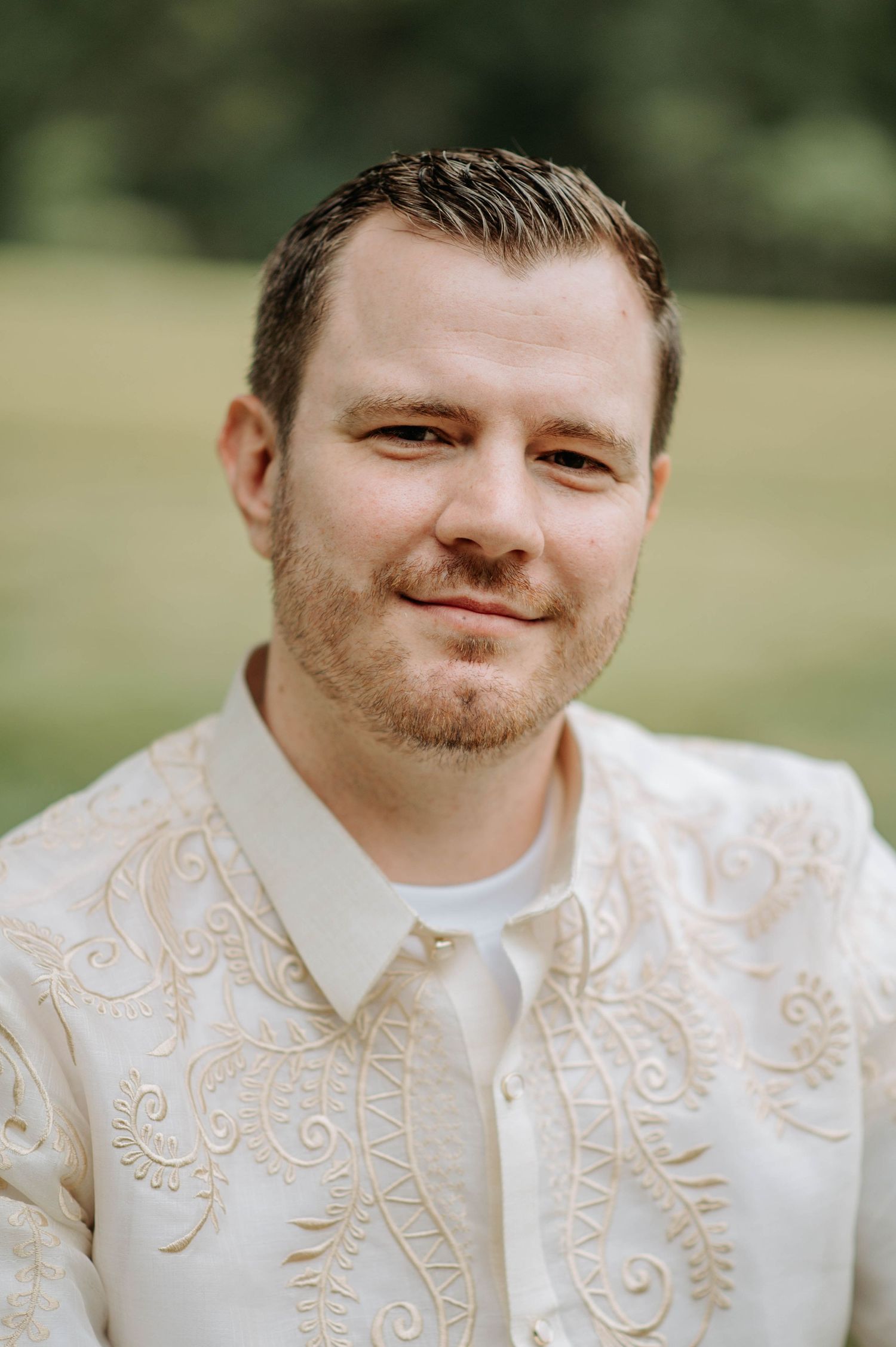 Wedding portrait in cream embroidered vest against natural outdoor background.