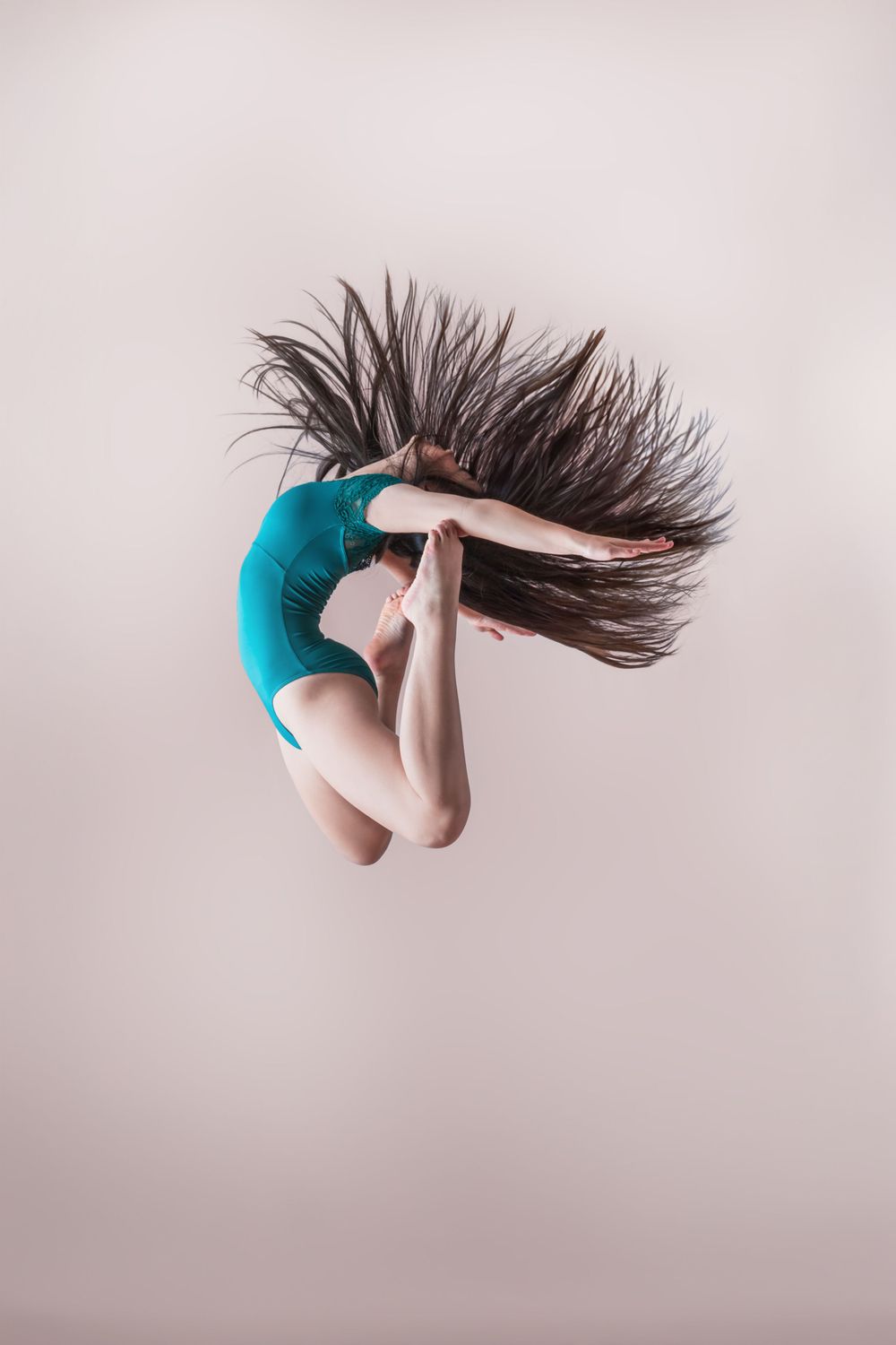 Dancer in teal leotard performing a dynamic jump with hair flowing through the air.
