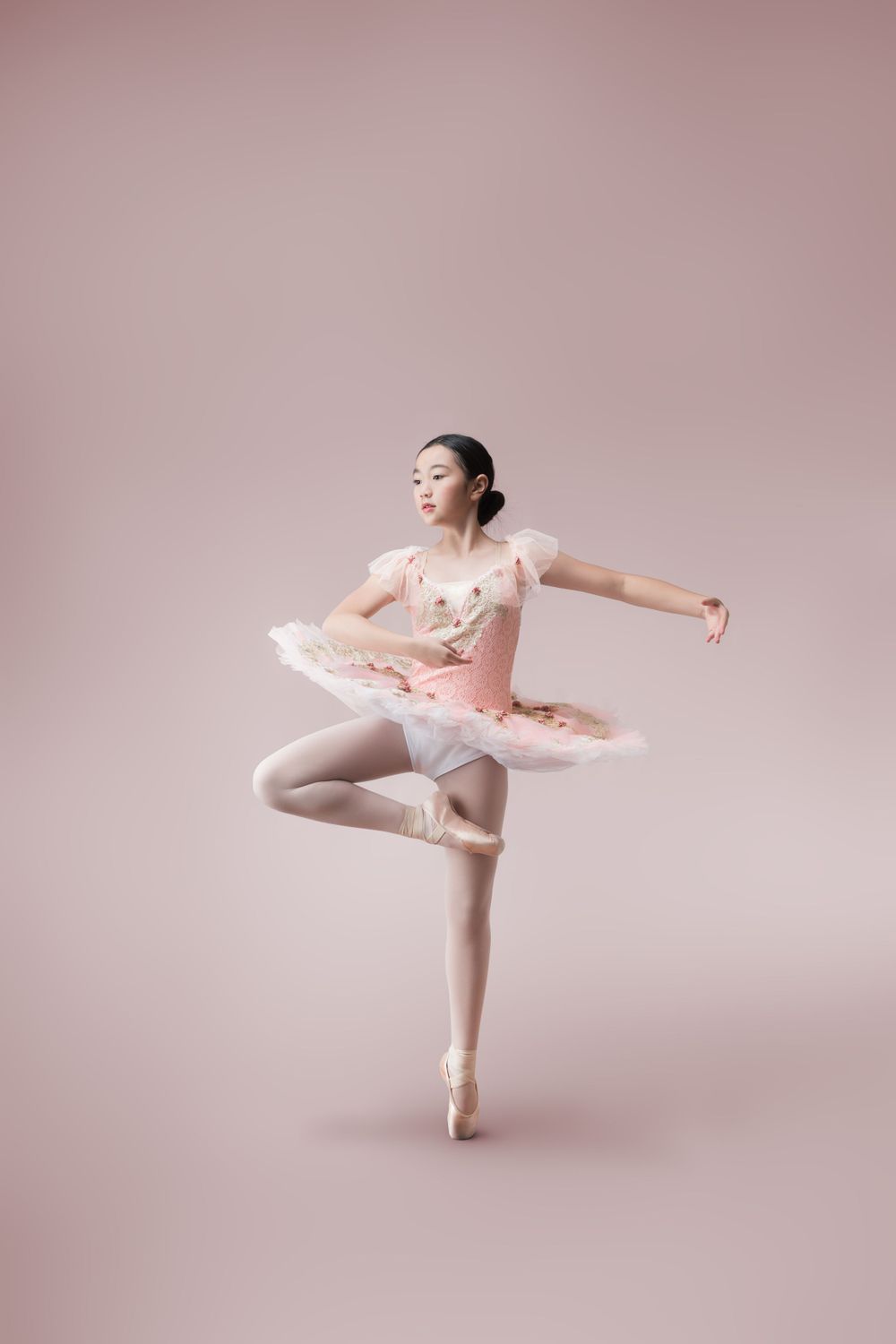 Ballet dancer in pink tutu performing a classical pose on pointe against pink background.