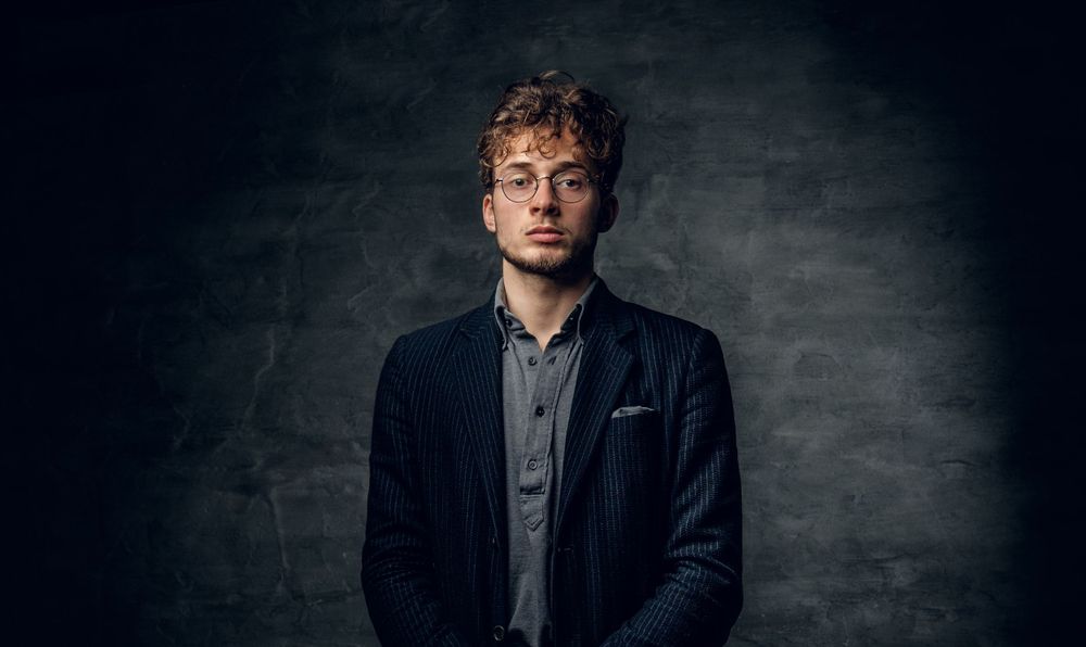 Dramatic studio portrait against dark textured wall with moody lighting.