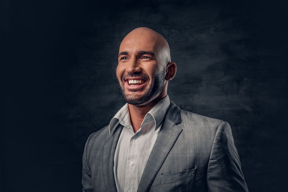 Professional headshot of person in grey suit against dark background.
