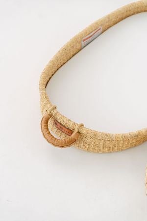 Curved natural woven rattan or jute accessory with metallic detail against white background.