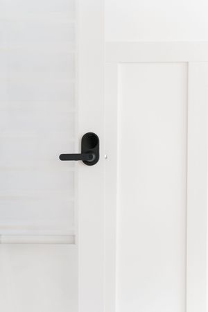 A modern black door handle on a minimalist white door against a bright white wall.