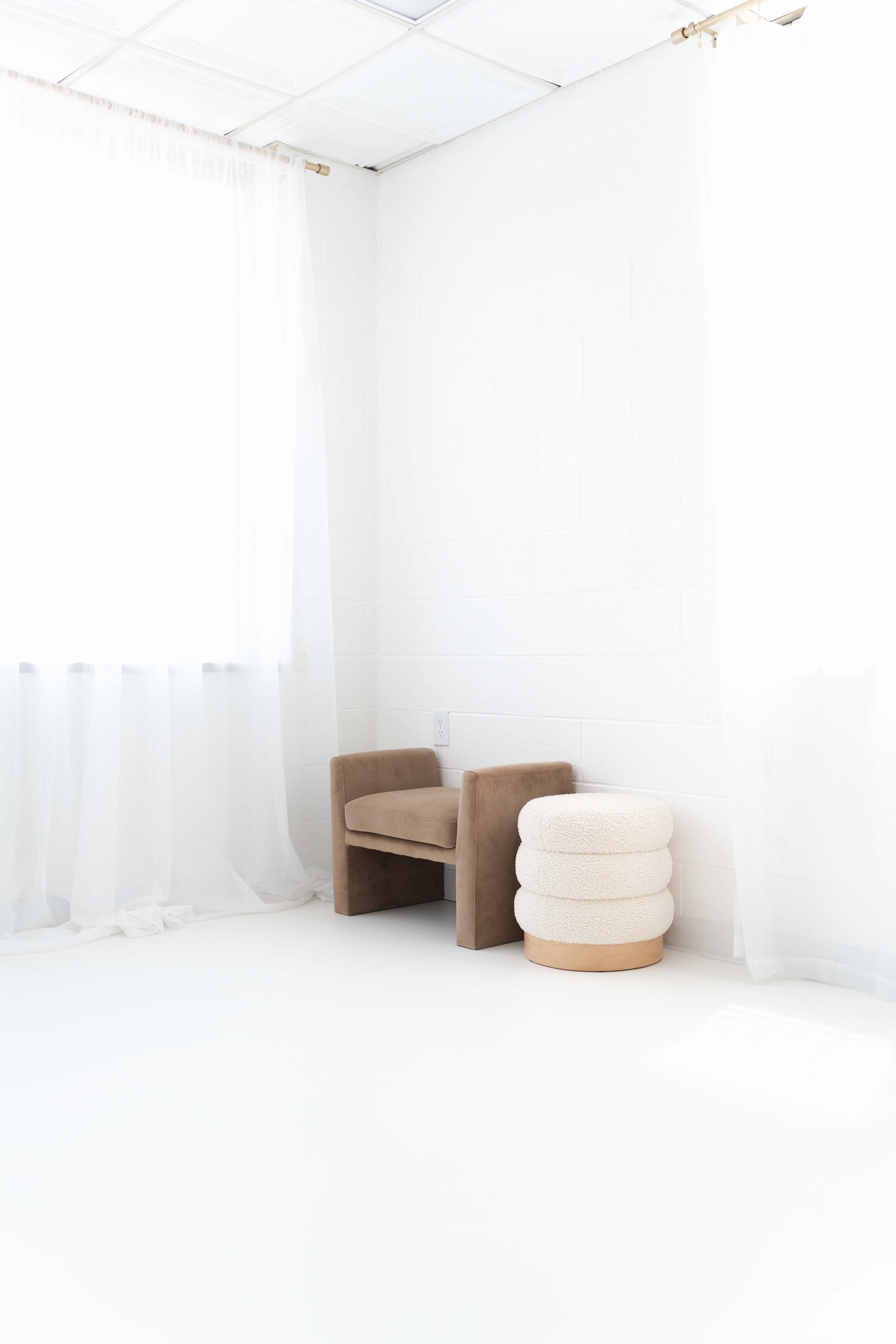 A minimalist white room interior with cardboard furniture pieces and soft white curtains filtering natural light.