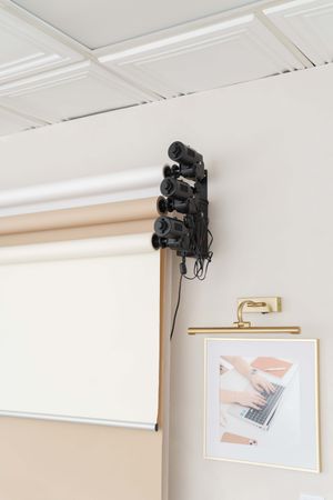 A wall-mounted stage light fixture installed near the ceiling of a white room with framed artwork displayed below it.