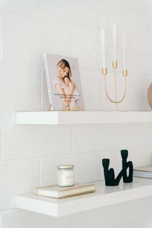 Minimalist white floating shelf display featuring decorative candle holders, books, and home decor items against a light wall.