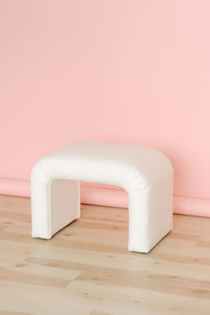 White curved bench seat against a pink wall on wooden flooring.