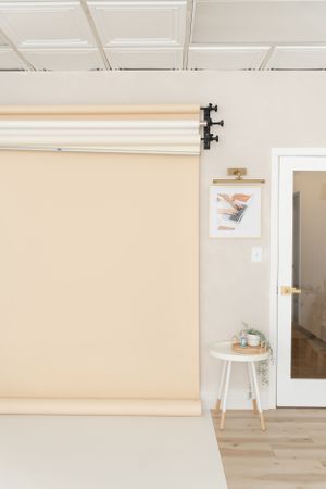 Clean photography studio interior with beige seamless backdrop, white ceiling, hardwood floor and small side table with decor.