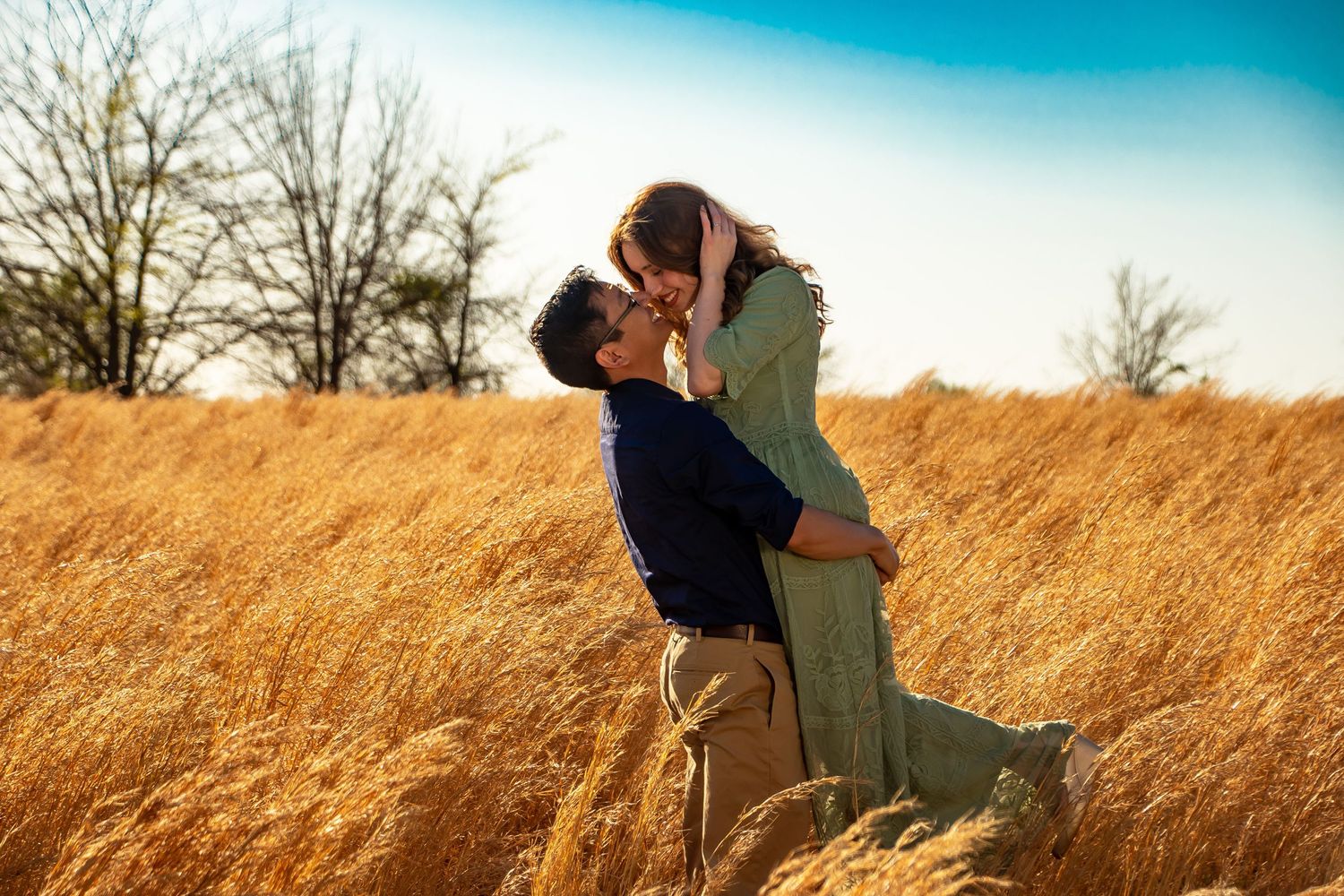 A couple shares a romantic moment in a golden wheat field during sunset.