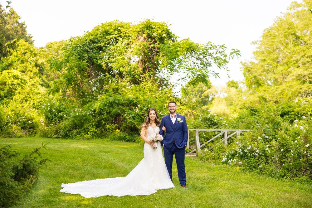 A couple poses together in a sunny garden setting with lush green foliage serving as a natural backdrop.