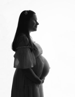 Black and white silhouette of a pregnant woman in an off-shoulder dress, cradling her baby bump in a studio.