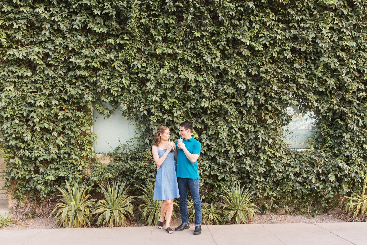Couple embracing against ivy covered wall during outdoor photo session.