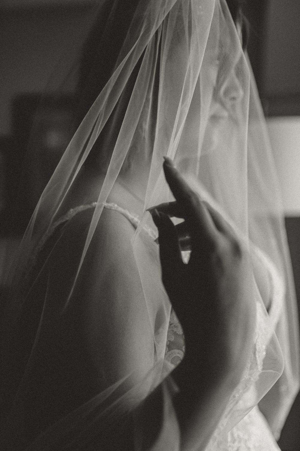 Black and white close-up of a bride adjusting her lace gown beneath a flowing veil.