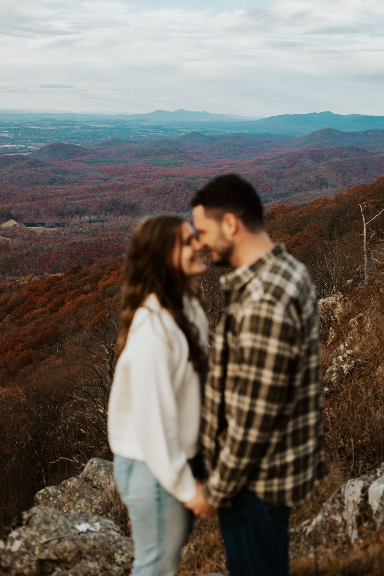 Couple holding hands on a mountain overlook surrounded by autumn foliage in the Appalachian Mountains.