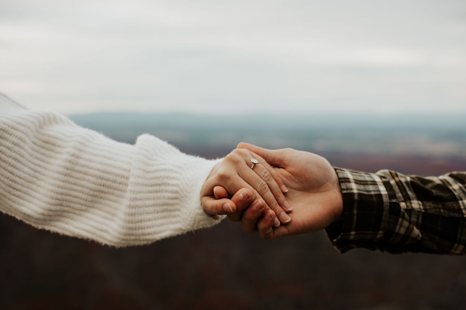 Two people holding hands outdoors, taken during an engagement photoshoot to highlight the ring.