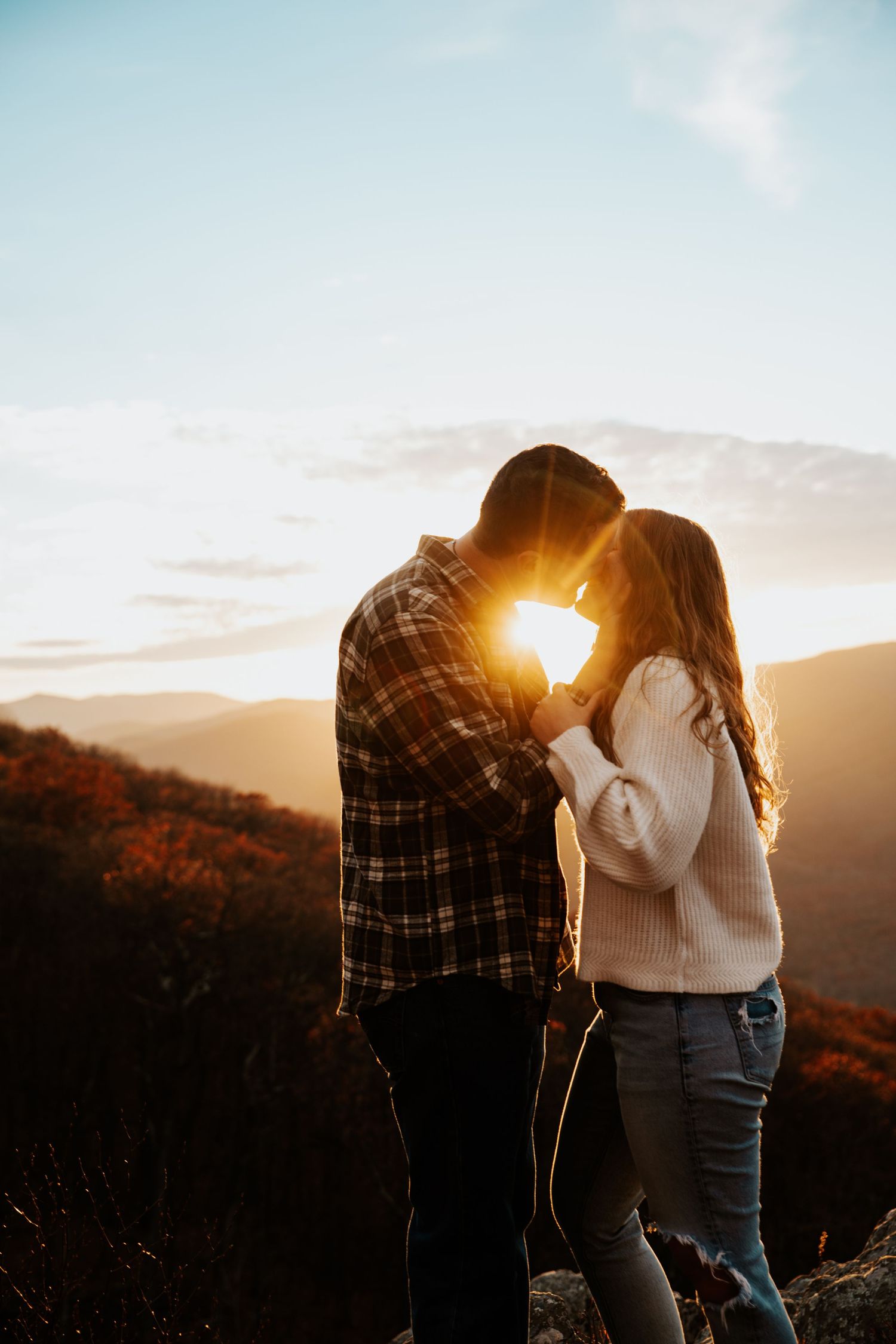 Couple sharing a romantic sunset moment on a mountain overlook surrounded by autumn foliage.
