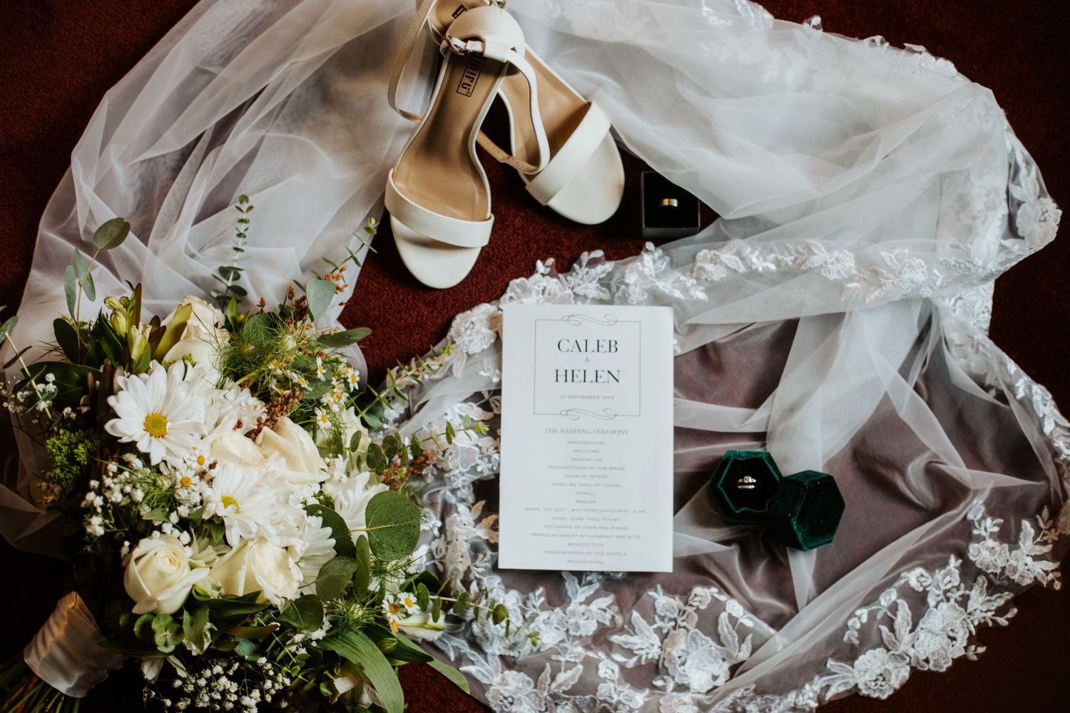 Wedding flat lay featuring invitation for Caleb and Helen, bridal veil, bouquet, and heels.