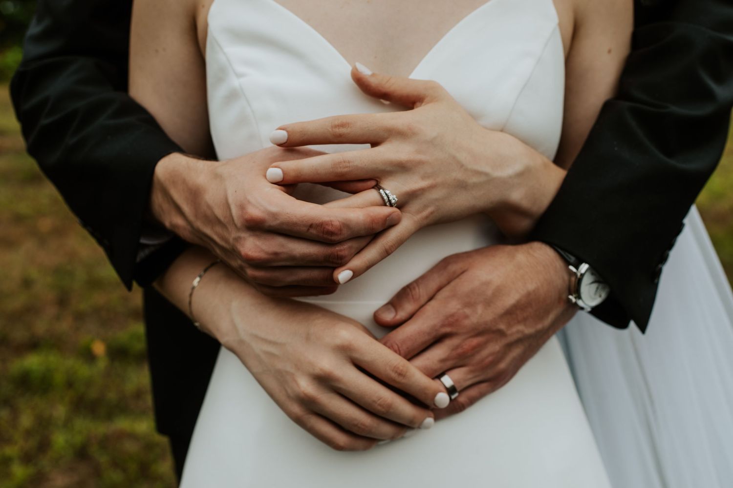 Wedding couple embracing, showing off their wedding rings and bands with clasped hands.