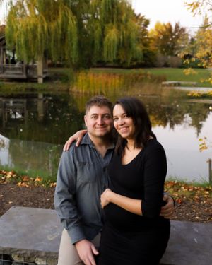 Couple embracing by autumn pond with weeping willow trees in background.