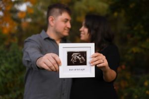 A couple holds up an ultrasound photo against an autumn background, sharing their pregnancy announcement.