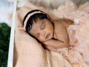 Peaceful newborn sleeping in soft peach fabric with delicate lace accents.