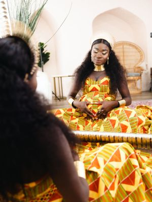 Woman in vibrant African print dress seated in peaceful meditation pose.
