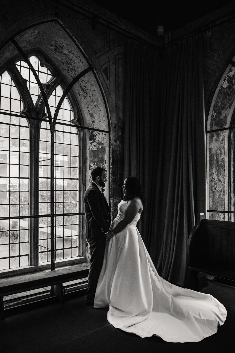 A dramatic black and white wedding photo series showing a bride in a flowing white gown against gothic arched windows.