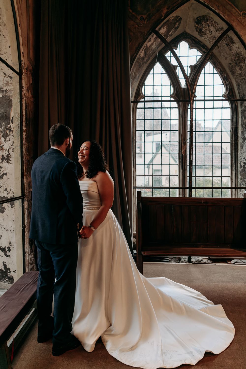 A couple shares an intimate moment in a gothic church interior with arched windows and dramatic lighting.