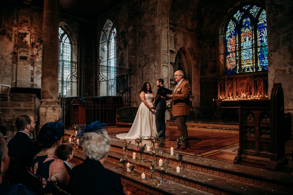 Gothic church interior with stained glass windows and candlelit aisle creating a moody, romantic atmosphere.