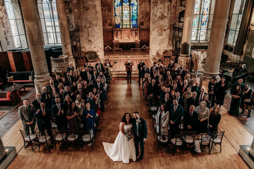 Wedding ceremony taking place in a historic stone chapel with stained glass windows and guests seated in wooden chairs.