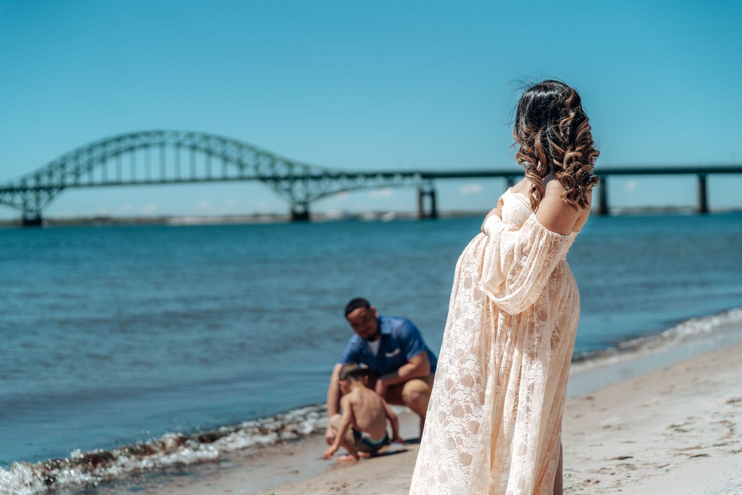 A dreamy beach scene with a flowing white dress and bridge silhouette in the background.