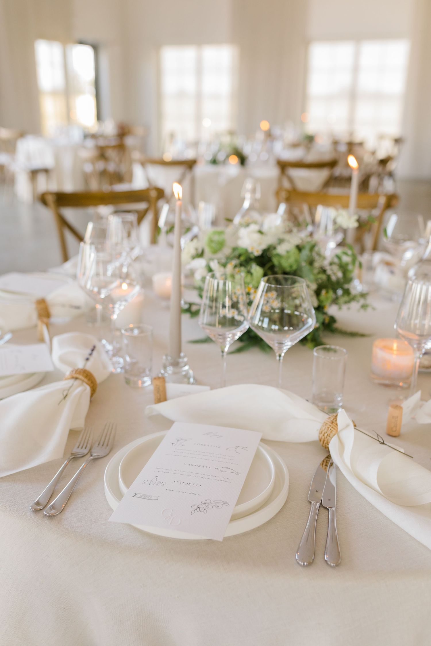 Elegant wedding table setting with white linens, candles, green floral centerpieces and crystal wine glasses.