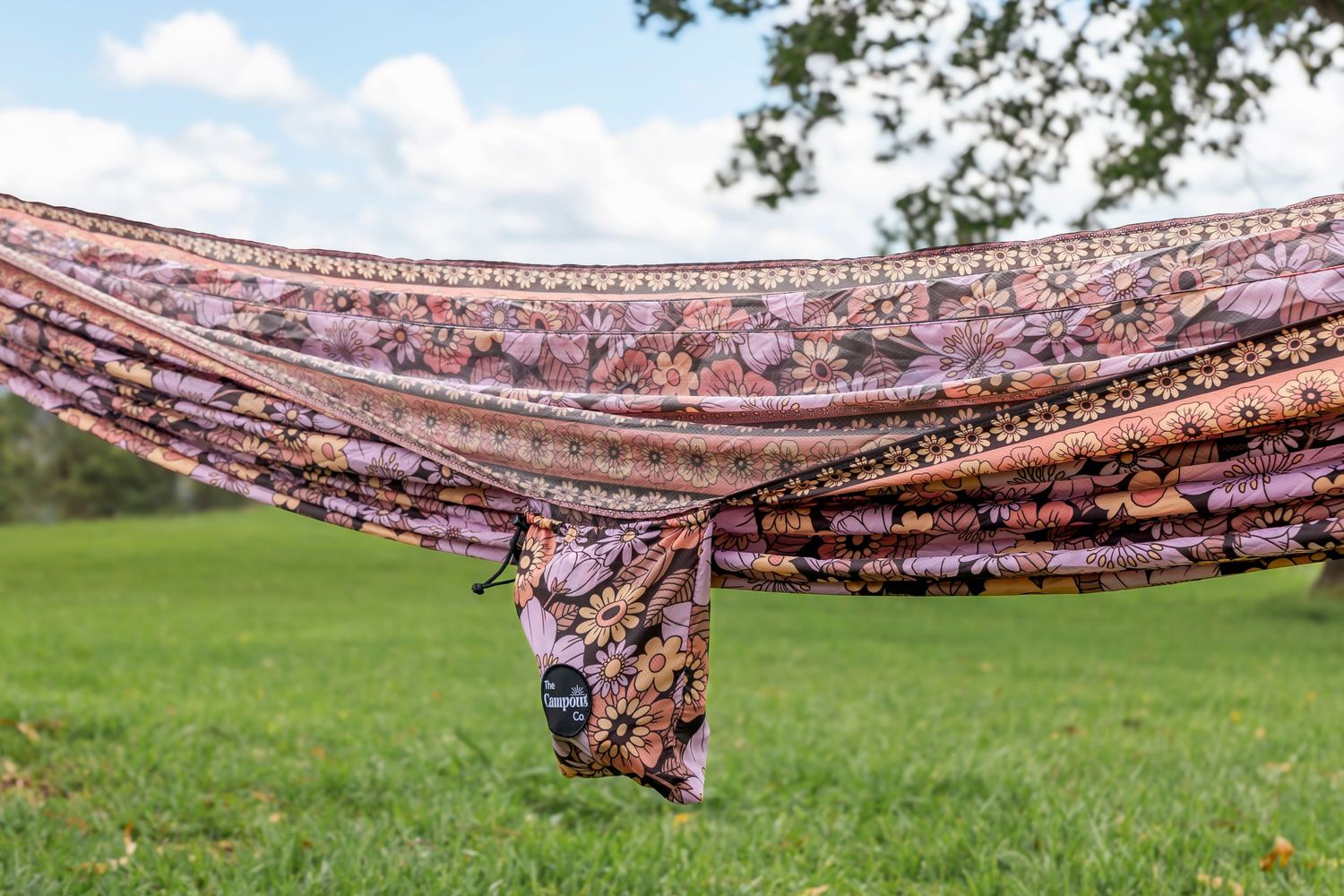 A patterned hammock with floral designs stretched across a grassy hilltop.