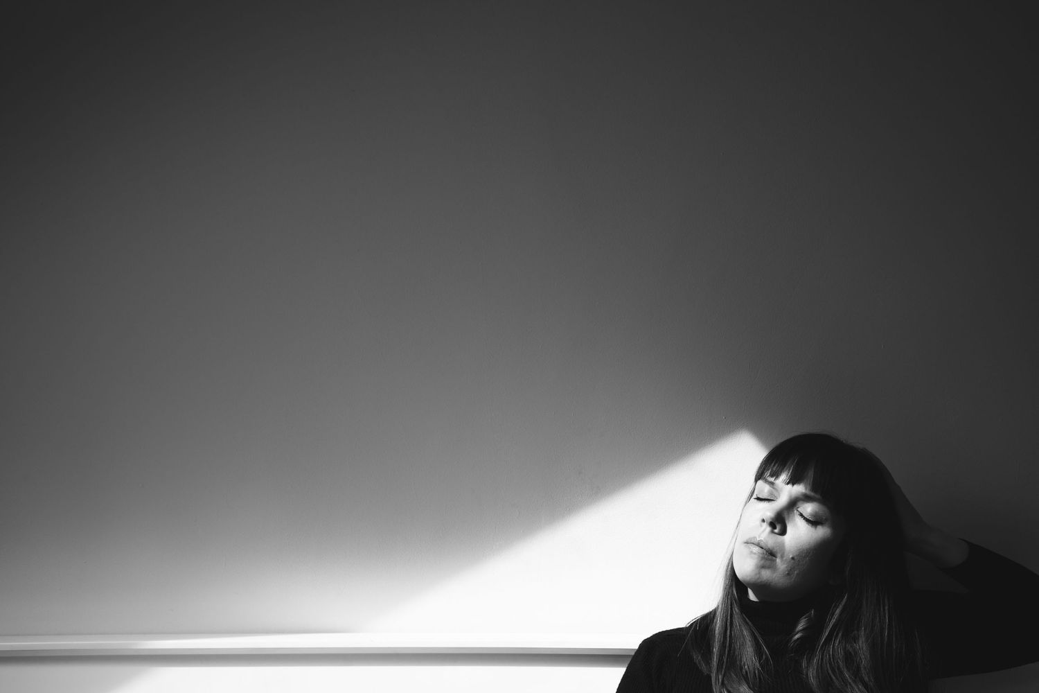 Artistic black and white portrait with dramatic lighting and shadow falling across a relaxed figure.