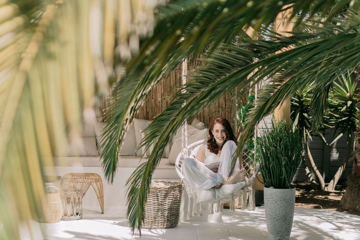Woman relaxing in a white chair surrounded by lush tropical palm trees in a bright space.
