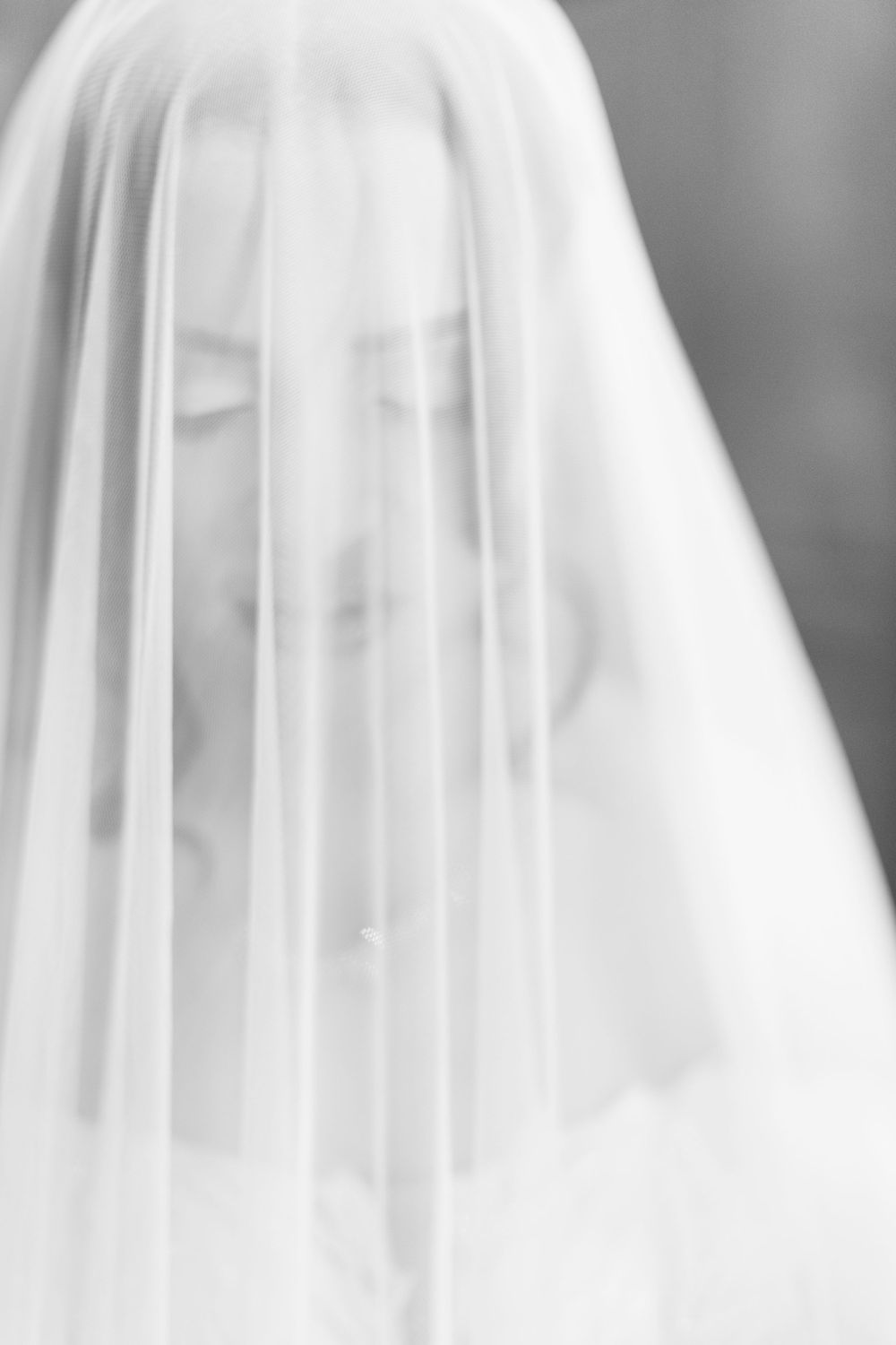 Soft focus black and white portrait of a bride behind a flowing veil.