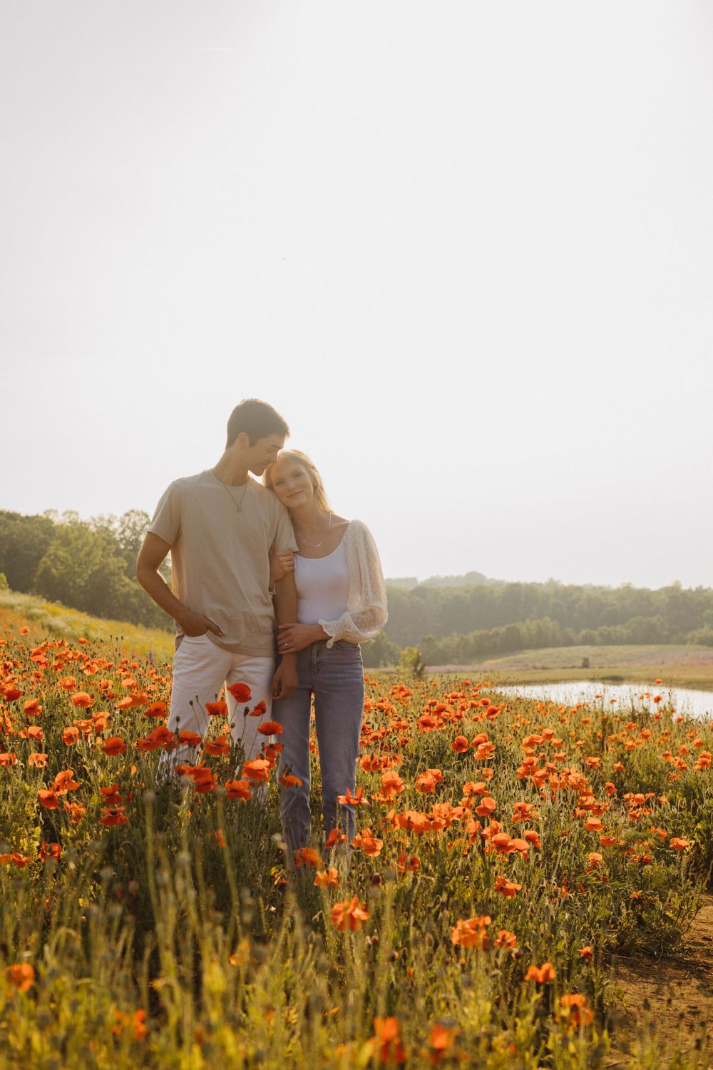 Couple walking through vibrant orange poppy field at sunset.