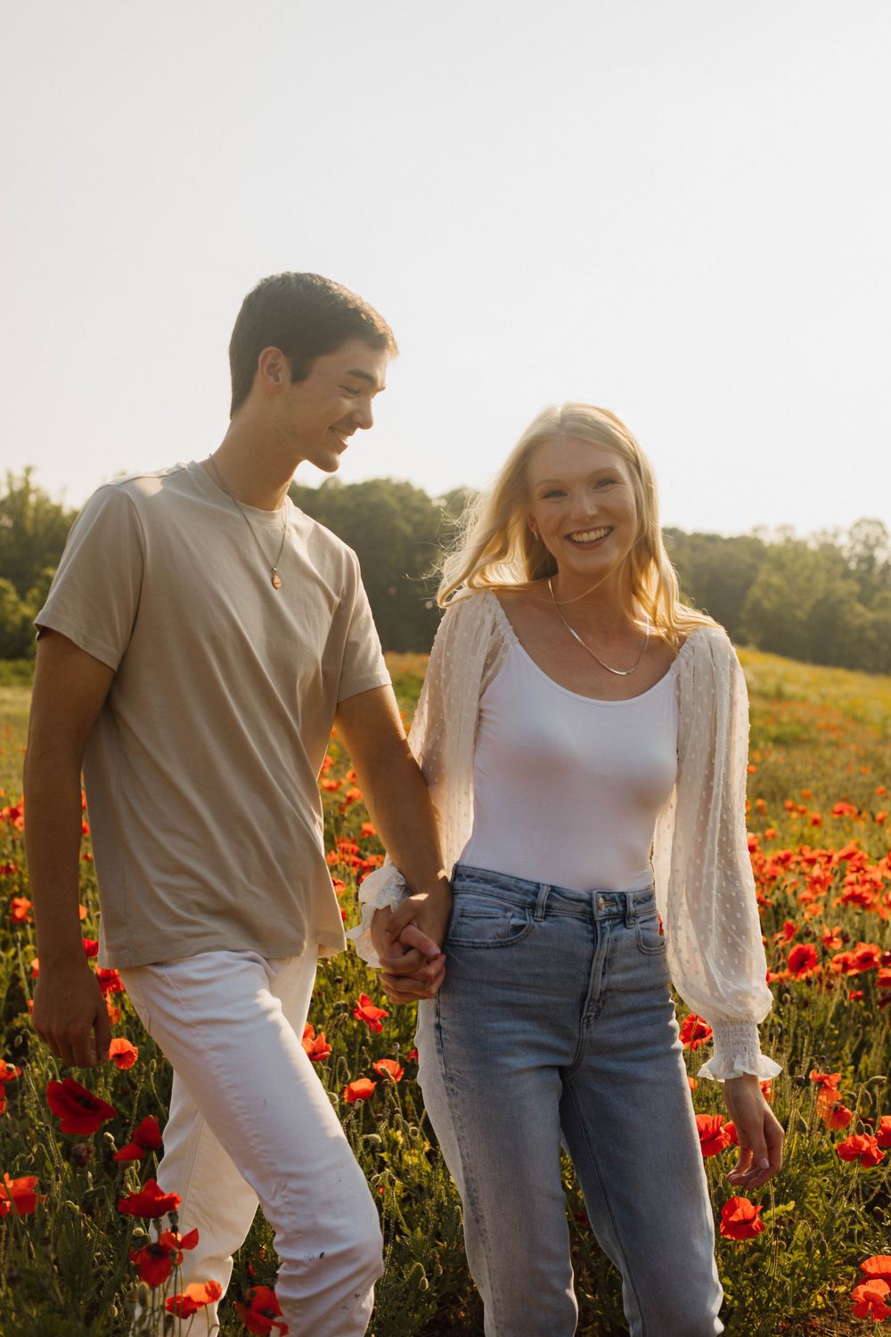 Couple laughing together in field of red poppies at sunset.