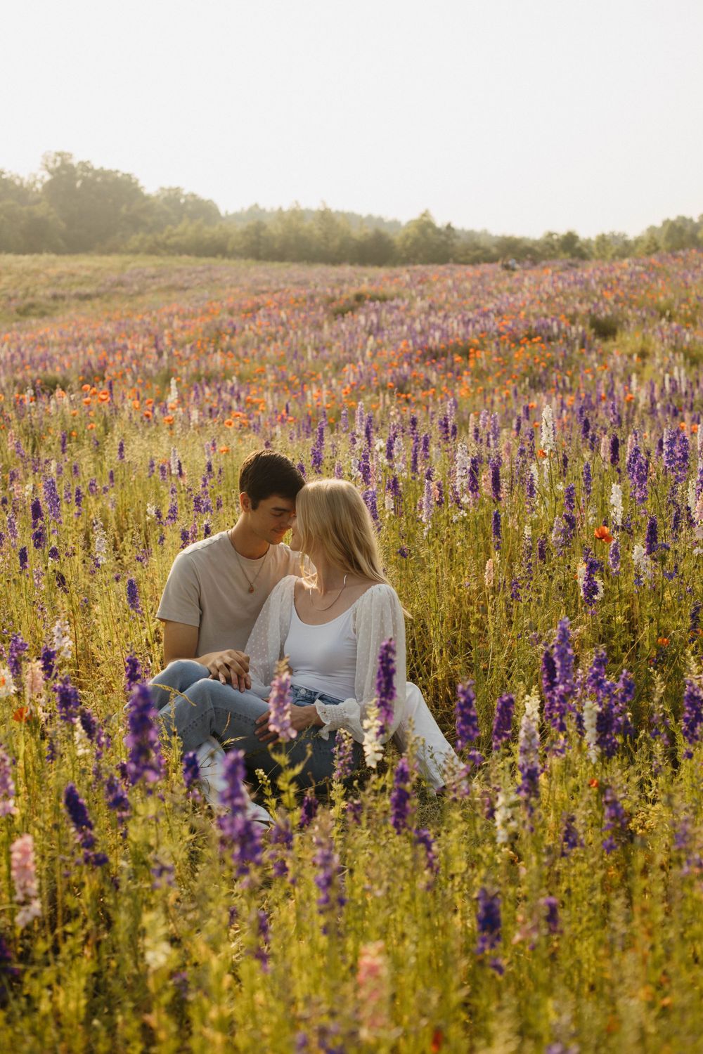Couple sitting together in a meadow filled with colorful summer wildflowers.