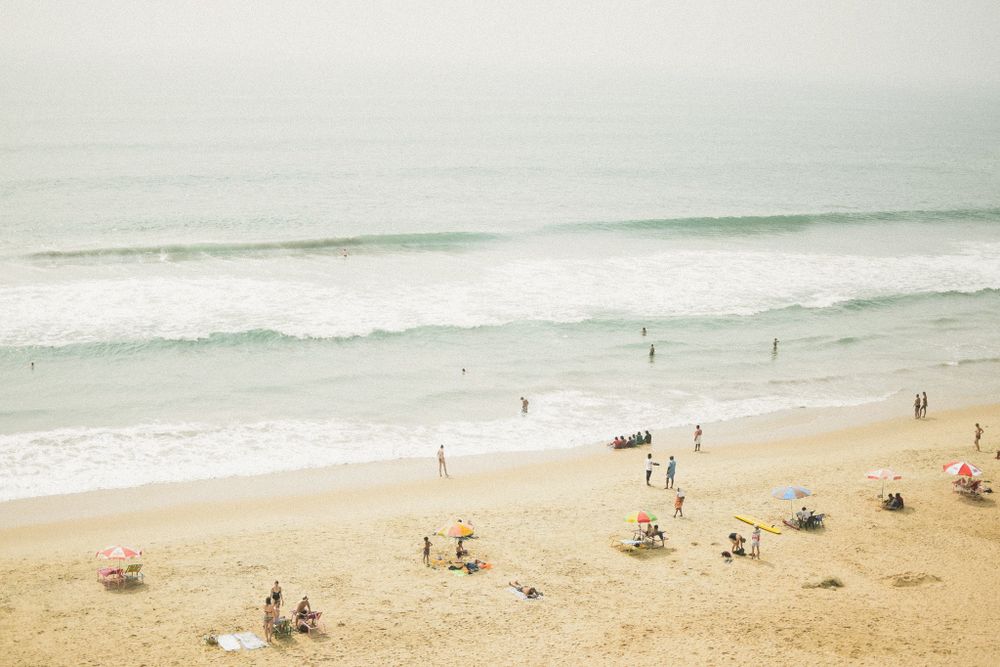 Aerial view of a sandy beach with scattered beachgoers and rolling waves.