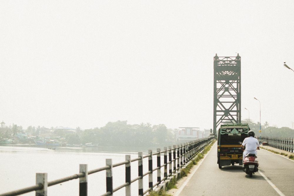 Metal bridge with railings stretches across a river with vehicles in the distance.